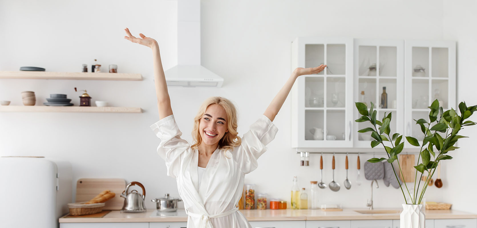 Happy woman with her arms raised celebrating life in her kitchen. Buy weed online in Canada from best online dispensary Low Price Bud.