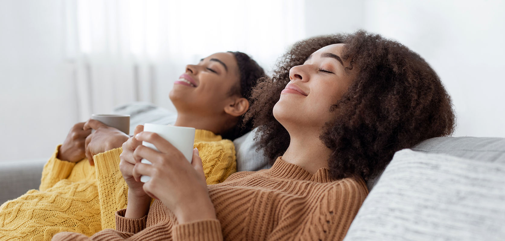 Two women friends relaxing on the sofa with coffee after buying weed online from mail order marijuana online dispensary Low Price Bud in BC.
