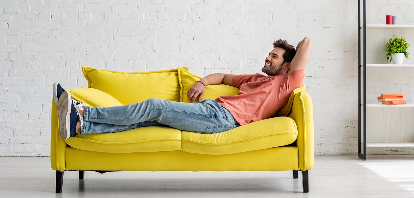 Happy man chilling at home on his yellow sofa after buying weed online from canadian online dispensary for cannabis canada. 